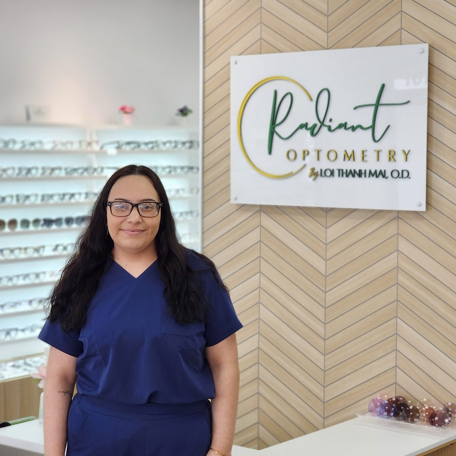 Jackie, optometric assistant at Radiant Optometry in Bellflower, CA, beside the office sign